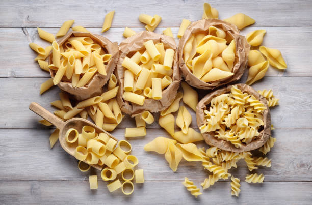 生パスタの品揃え:ペン、シェル、リガトーニ、フジッリ、イカの木の背景、トップビュー。 - pasta directly above fusilli food ストックフォトと画像