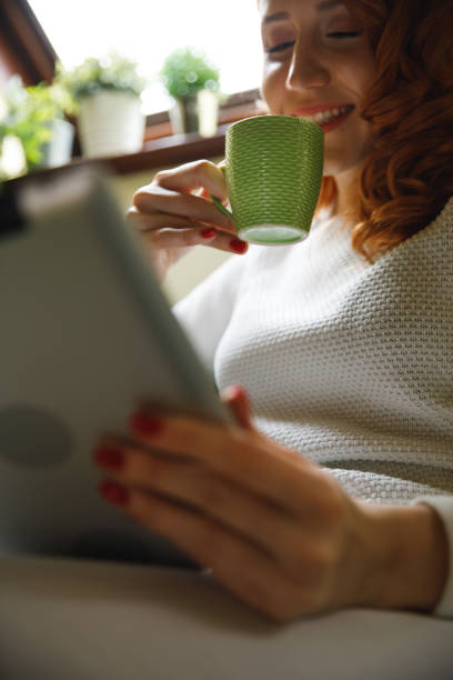 istock Portrait of smiling young redhead using digital tablet and sipping coffee 1390349313