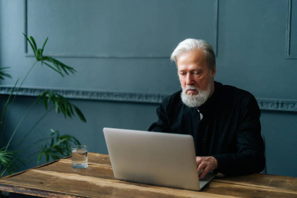 istock Portrait of focused gray-haired mature elderly man working on computer with electronic document, considering information. 1390351115