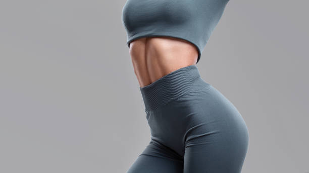 Close-up belly of a young girl on a gray background. portrait of a girl in sportswear with strong abdominal muscles. Fitness woman with abs. Close-up belly of a young girl on a gray background. portrait of a girl in sportswear with strong abdominal muscles. Fitness woman with abs. tanned body stock pictures, royalty-free photos & images