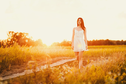 Beautiful young woman walking in flower park in white dress at sunset background, Healthy Lifestyle outdoor relaxation Summer scenes  Soft focus
