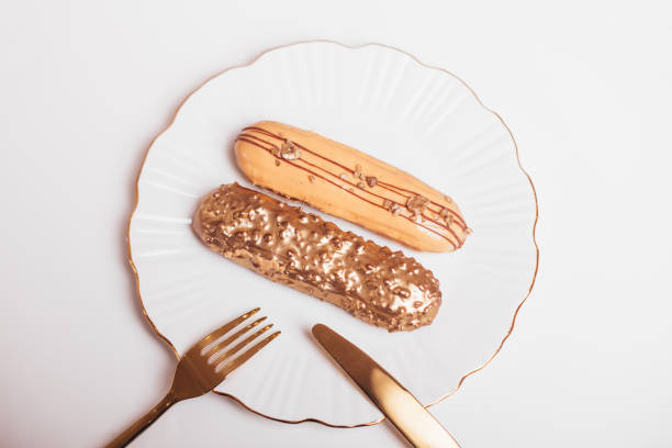 Beautiful golden colored eclairs on plate, with knife and fork, on white background