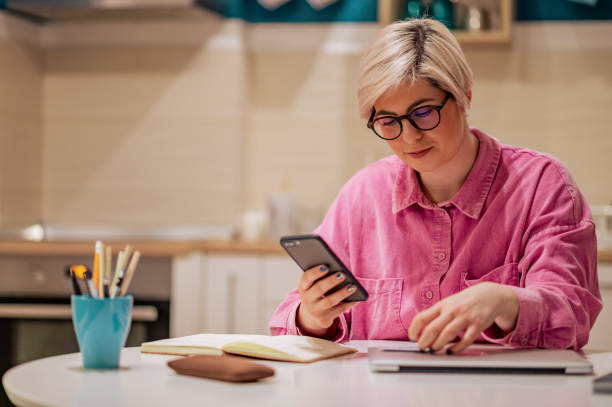 istock Short haired woman using smartphone in the kitchen at home 1390363027
