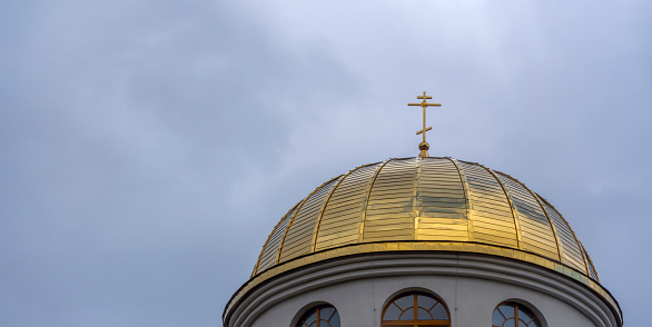 Close-up view of golden yellow dome of church with orthodox cross on dramatic sky background. Space for text. Worship concepts.