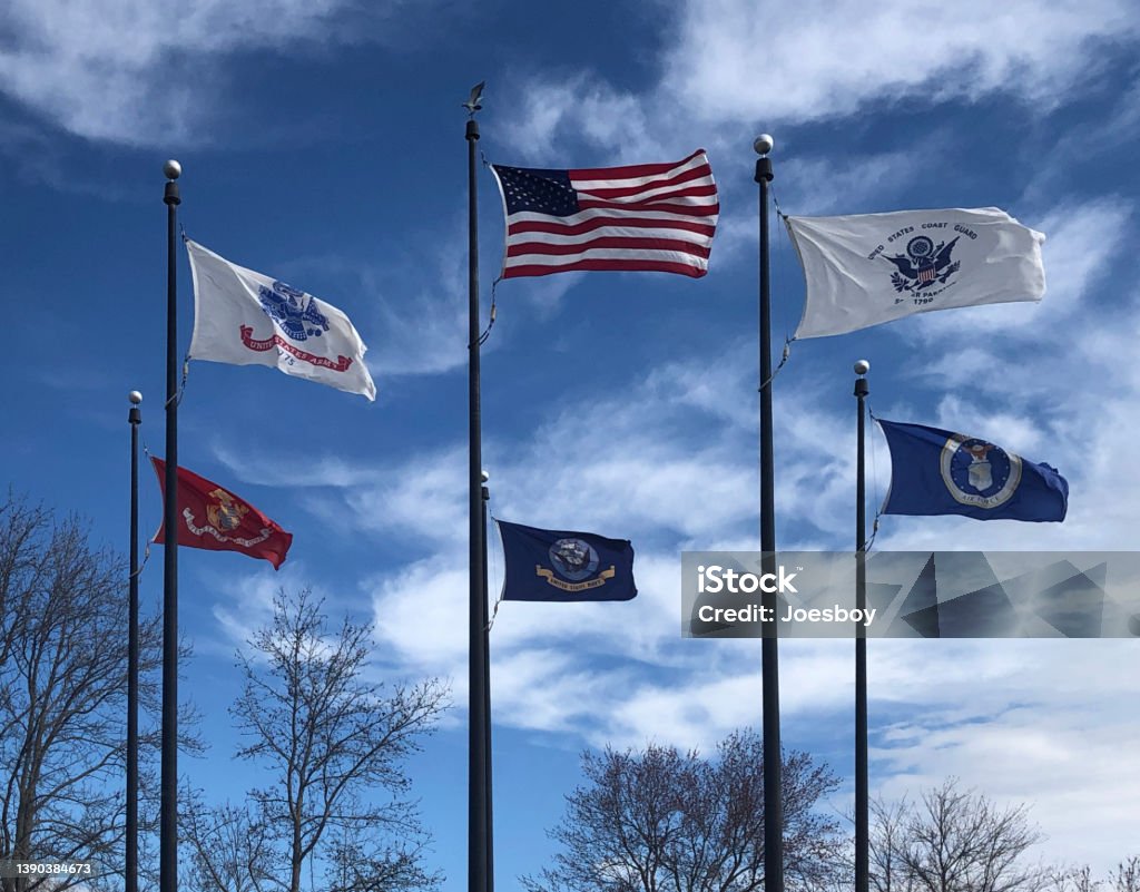Military Memorial Flag Array The flags of all branches of the US military encircle the US flag at a veterans memorial public  park near Ocean City, MD with a stiff wind blowing them out straight US Military Stock Photo