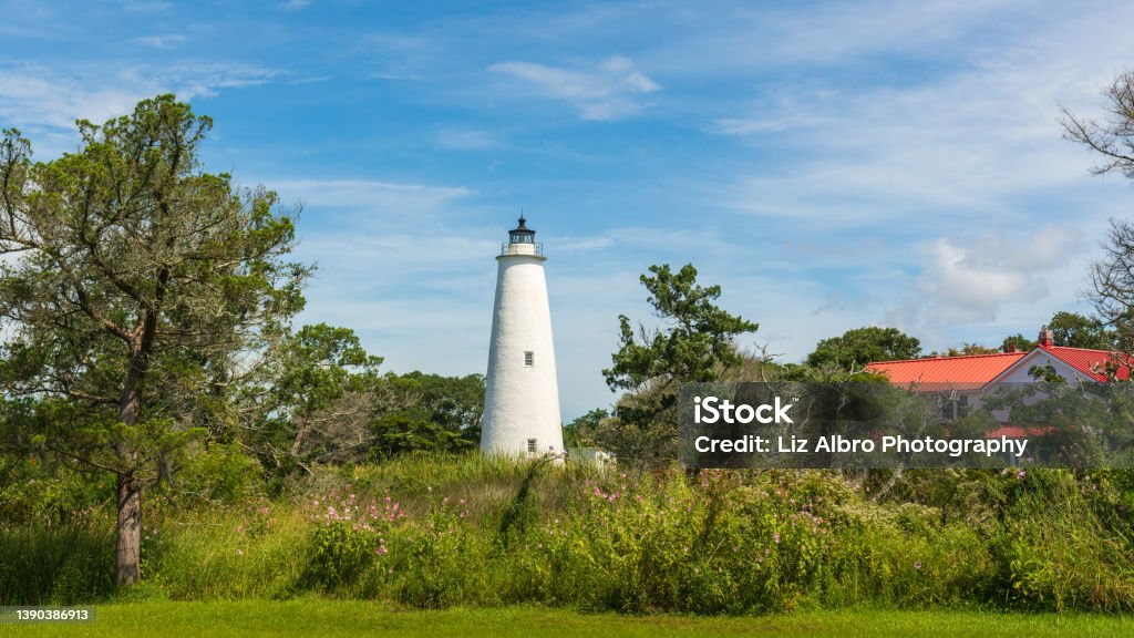 Ocracoke lighthouse on a summer morning with green marsh and red-roofed lighthouse keeper's house. Ocracoke Light is the oldest operating light station in North Carolina and the second oldest lighthouse still standing in the state. Ocracoke Island Stock Photo
