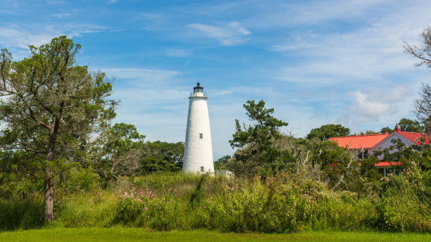 Ocracoke lighthouse on a summer morning with green marsh and red-roofed lighthouse keeper's house. Ocracoke Light is the oldest operating light station in North Carolina and the second oldest lighthouse still standing in the state. ocracoke lighthouse stock pictures, royalty-free photos & images