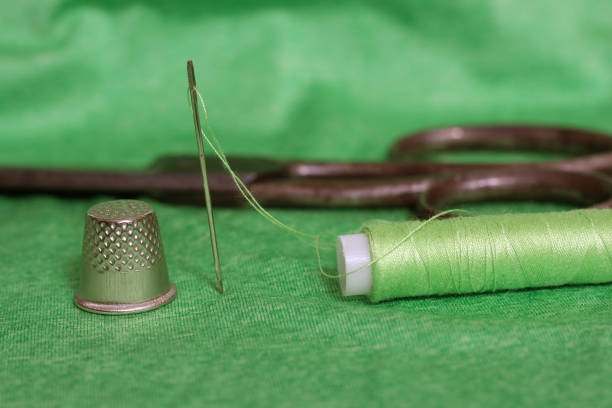 Spool of Green Thread, Thimble and Needle on Green Fabric Close up