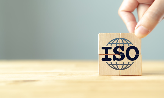 ISO standards quality control certification concept. Quality warranty and assurance.  Hand puts wooden cubes with ISO and smart globe icons on grey background and copy space. Modern ISO banner.