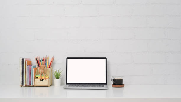 istock Front view computer laptop, coffee cup and stationery on white table against brick wall. 1390407598