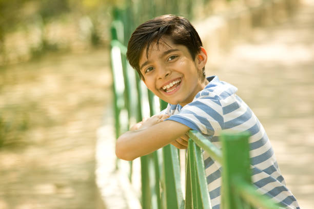 Portrait of cheerful boy leaning on fence at park