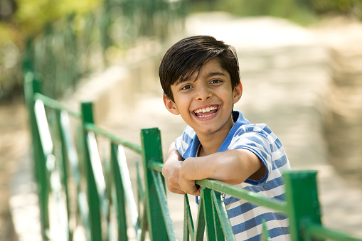 Portrait of cheerful boy leaning on fence at park