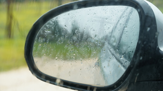 Blurred rain drops on a car window with the mirror in the background. Close up
