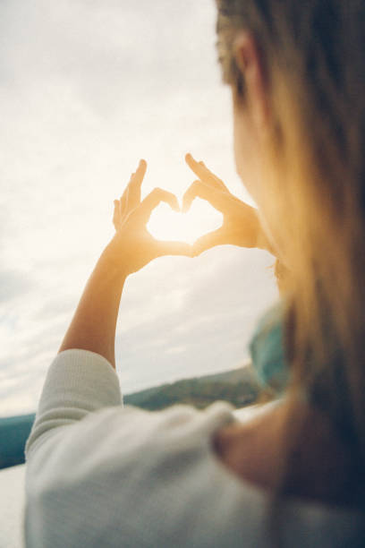 Nice woman making heart shape with fingers on sailboat on sailboat during sailing. Model released.