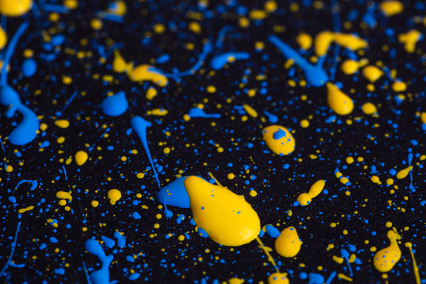 Blue and yellow paint drops on black canvas. Ukrainian flag concept .