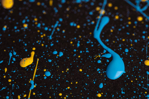 Blue and yellow paint drops on black canvas. Ukrainian flag concept .
