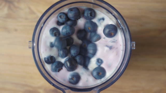 Running blender mixing blueberries and milk, making a shake, top view