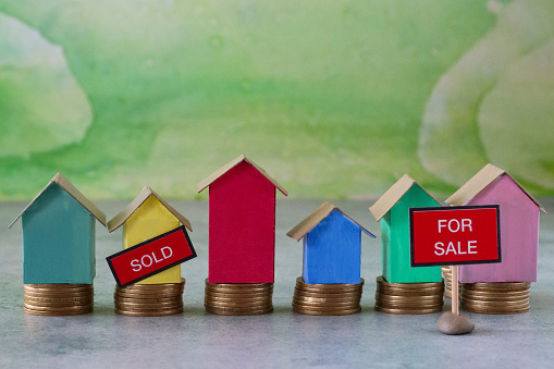Stock photo showing a close-up view of row of blue, red, green, pink and yellow cardboard houses stood on stacks of coins. This is a family finances, real estate and holiday savings concept picture.