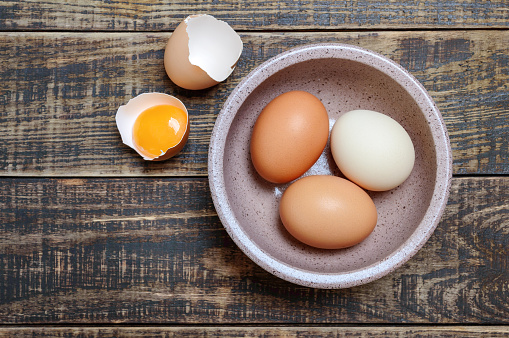Bowl of fresh raw chicken eggs on wooden background, top view.