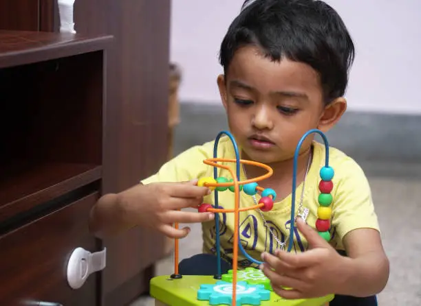Photo of an indian baby boy engaged with a bead puzzle toy, developmental activity milestone concept image