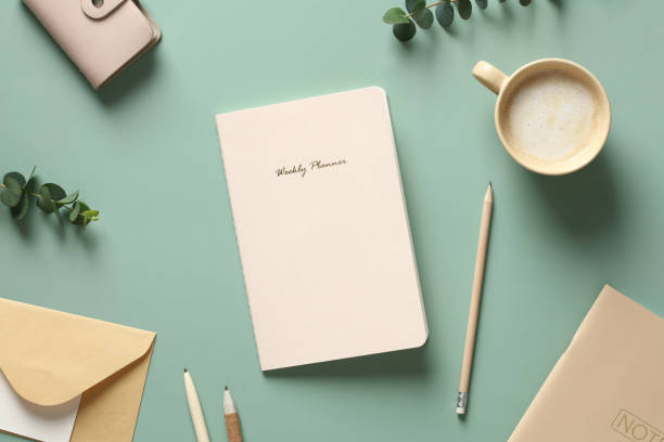 istock Flat lay weekly planner, cup of coffee, pencil, envelope, paper notebook, accessories on green table. Home office desk, feminine workspace. 1390437332