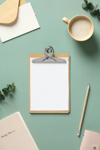 istock Blank clipboard, cup of coffee, paper notebook, envelopes, eucalyptus leaves on green background. Flat lay, top view, copy space. 1390437333