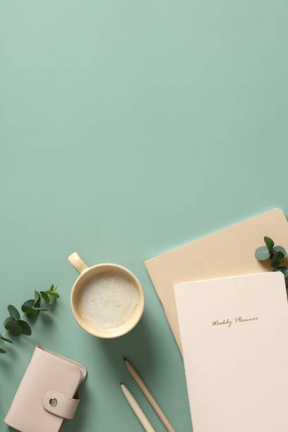 istock Aesthetics workspace with cup of coffee, paper notebooks, feminine accessories and eucalyptus leaves on green table. Flat lay, top view. 1390438517