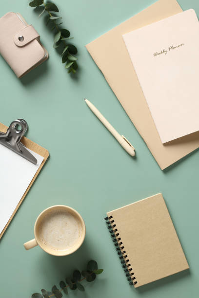 istock Elegant home office desk table top view. Feminine workspace with cup of coffee, paper notebook, notepad, clipboard, stationery on green background 1390438757