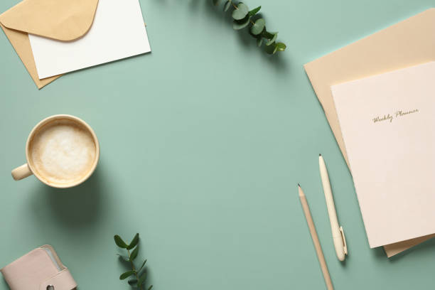 istock Elegant feminine workspace with cup of coffee, notebooks, eucalyptus leaves on green table. Flat lay, top view. 1390438839