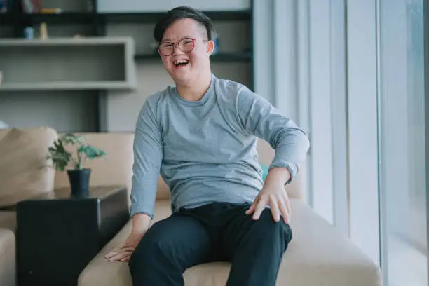 Photo of portrait Asian Chinese down syndrome young man looking at camera smiling in living room