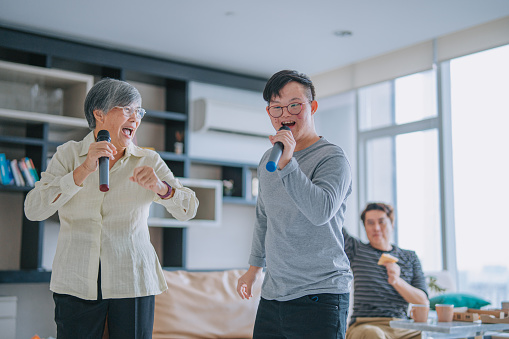 Asian Chinese down syndrome young man singing dancing with his grandmother having fun in living room during weekend