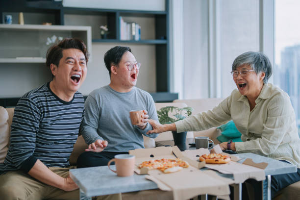 asiatische chinesische mehrgenerationenfamilie mit down-syndrom-enkel, der am wochenende pizza fast food im wohnzimmer auf dem sofa genießt - grandmother senior adult child multi generation family stock-fotos und bilder