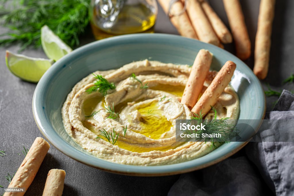 Tasty and homemade hummus with breadsticks, olive oil and dill. Tasty and homemade hummus with breadsticks, olive oil and dill. Hummus served with breadsticks and olive oil. Hummus - Food Stock Photo