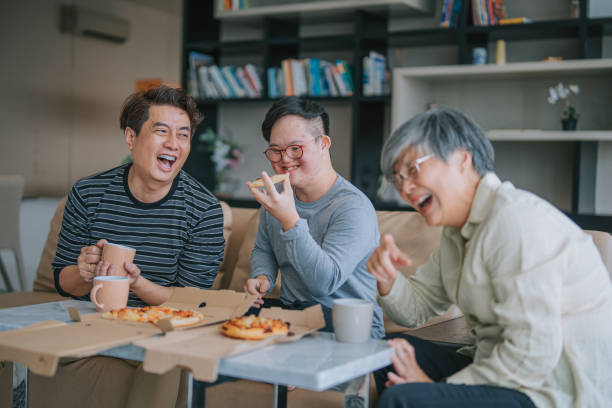 asiatische chinesische mehrgenerationenfamilie mit down-syndrom-enkel, der am wochenende pizza fast food im wohnzimmer auf dem sofa genießt - grandmother senior adult child multi generation family stock-fotos und bilder