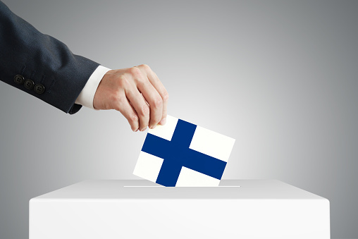 Man putting a voting ballot into a box with Finnish flag.