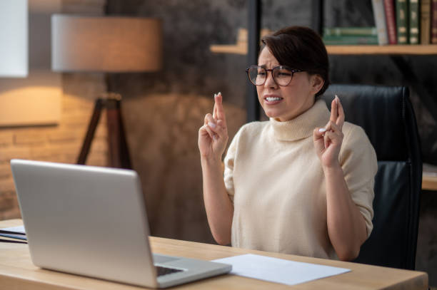 An excited woman sitting at the laptop with her fingers crossed stock photo