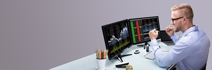 Excited Young Male Stock Market Broker Looking At Graph On Computer At Workplace