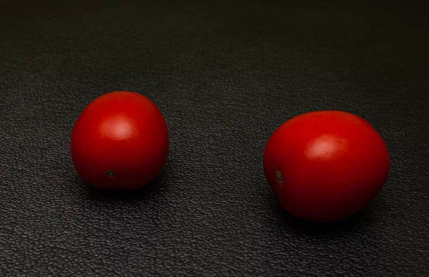 黒い背景に横たわる2つの新鮮な赤いトマト - plum red black food ストックフォトと画像