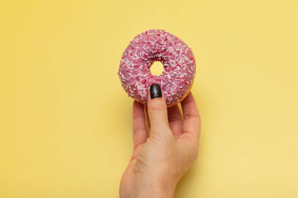 istock female hand holding donut on yellow green background 1390453557