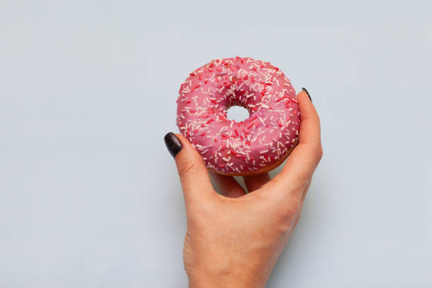 istock female hand holding donut on blue green background 1390453606