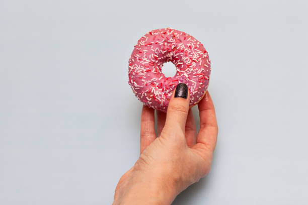 istock female hand holding donut on yellow green background 1390453609