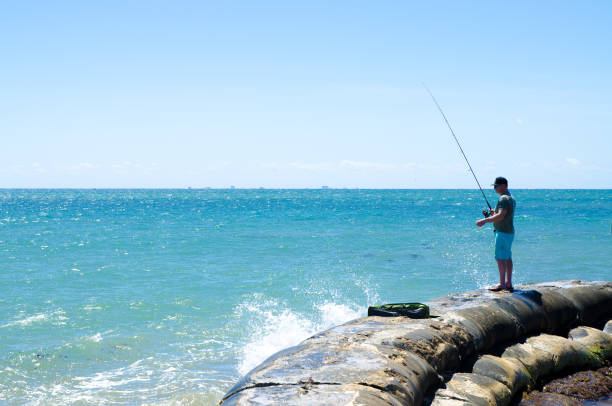 Fisherman on a dyke over Caribbean sea in Playa del Carmen during day of March