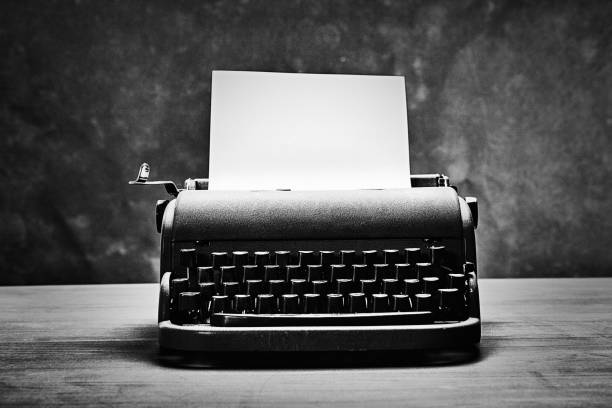 Antique typewriter from the mid-20th century with a blank page of paper ready for a novel Old-fashioned typewriter sitting on a desk, with copy space on the blank paper and on the background. typewriter stock pictures, royalty-free photos & images
