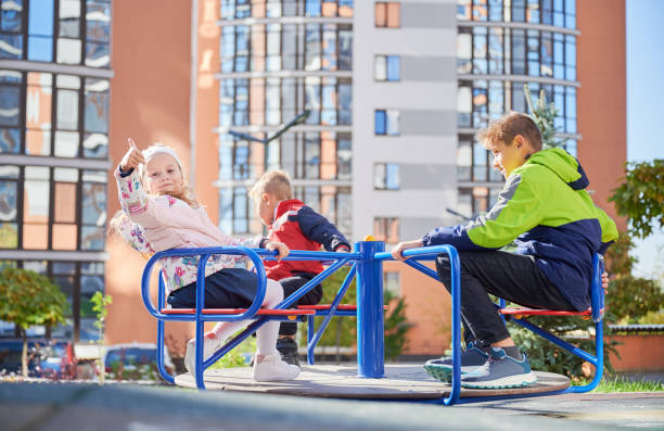 Three little kids playing on merry-go-round outdoors in spring.