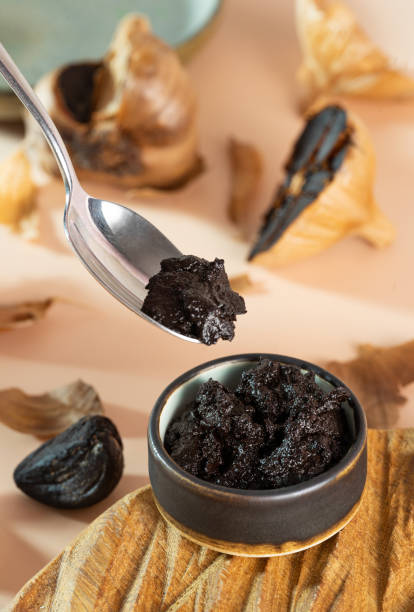 istock Spoon with aioli and clay ceramic bowl with black garlic paste on a handmade wooden plate. Fermented garlic bulb in the background. Healthy nutrition, fermented food, selective focus 1390468387
