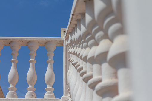 A street of modern villas with teracotta and beige walls sits behind a white wooden fence against the backdrop of a clear sky. Luxury vacation concept.