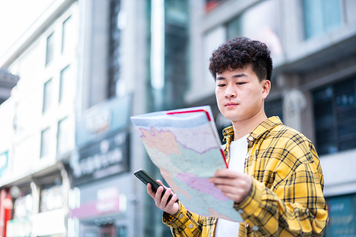 Asian young handsome man is using map to find travel destination in city street