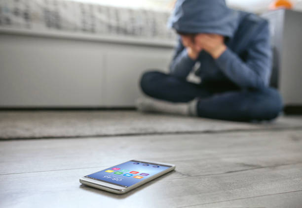 Teenager boy crying desperate for bullying with mobile lying on the floor in foreground stock photo
