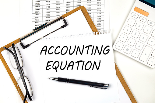 Text ACCOUNTING EQUATION on white paper on clipboard with chart and calculator