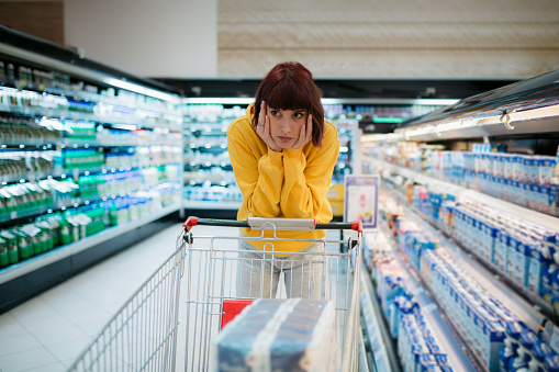 Upset woman in a supermarket with an empty shopping trolley. Crises, rising prices for goods and products. Woman shopping at the supermarket.